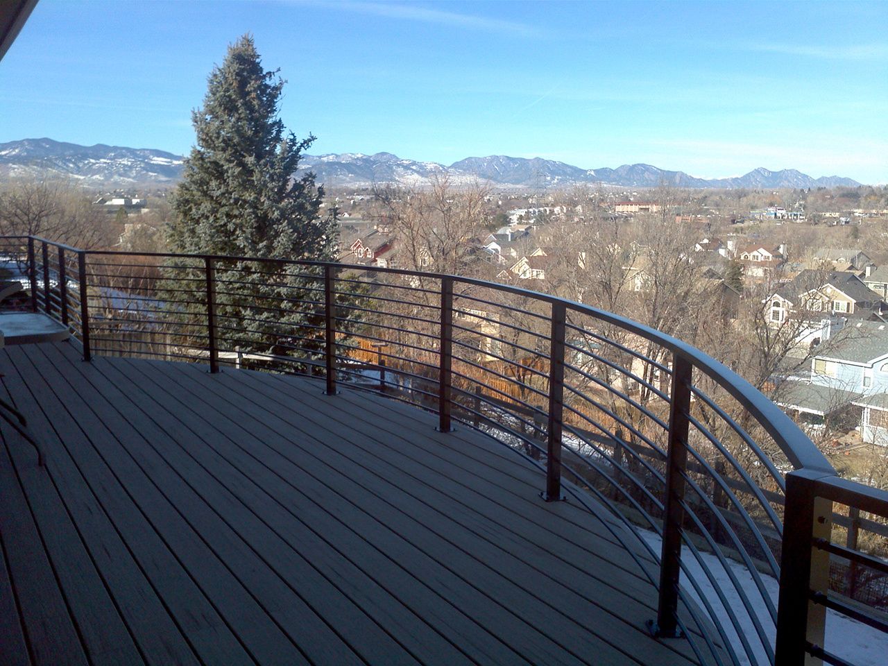 A wooden deck with a metal railing overlooking a city and mountains.