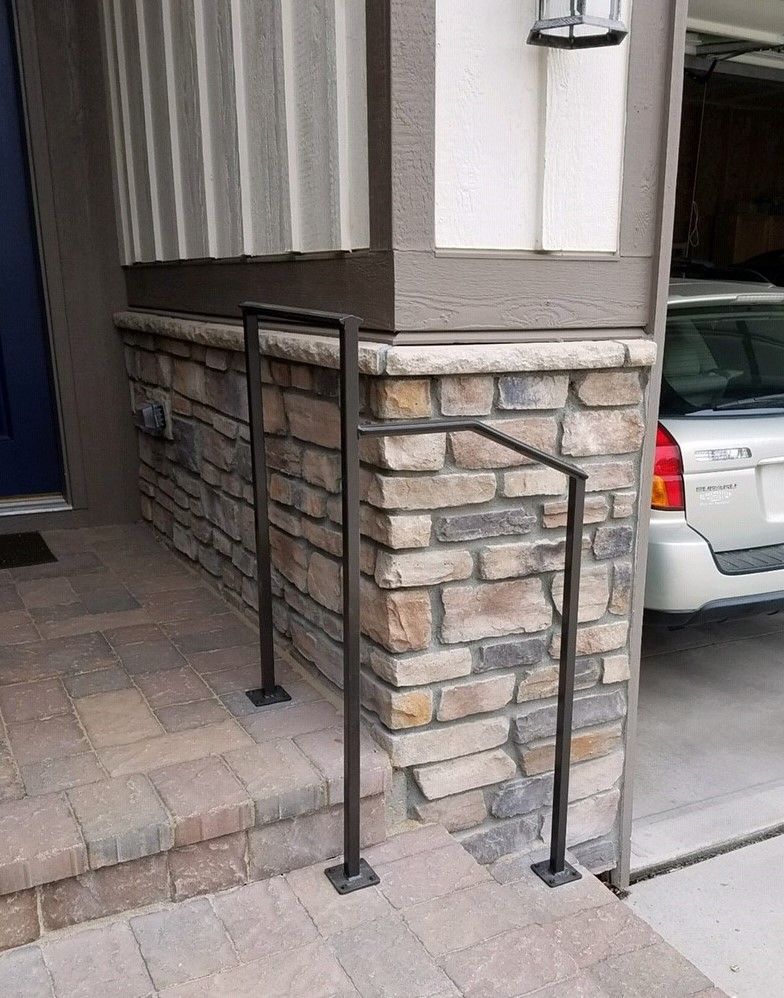 A car is parked in front of a brick building with a railing.