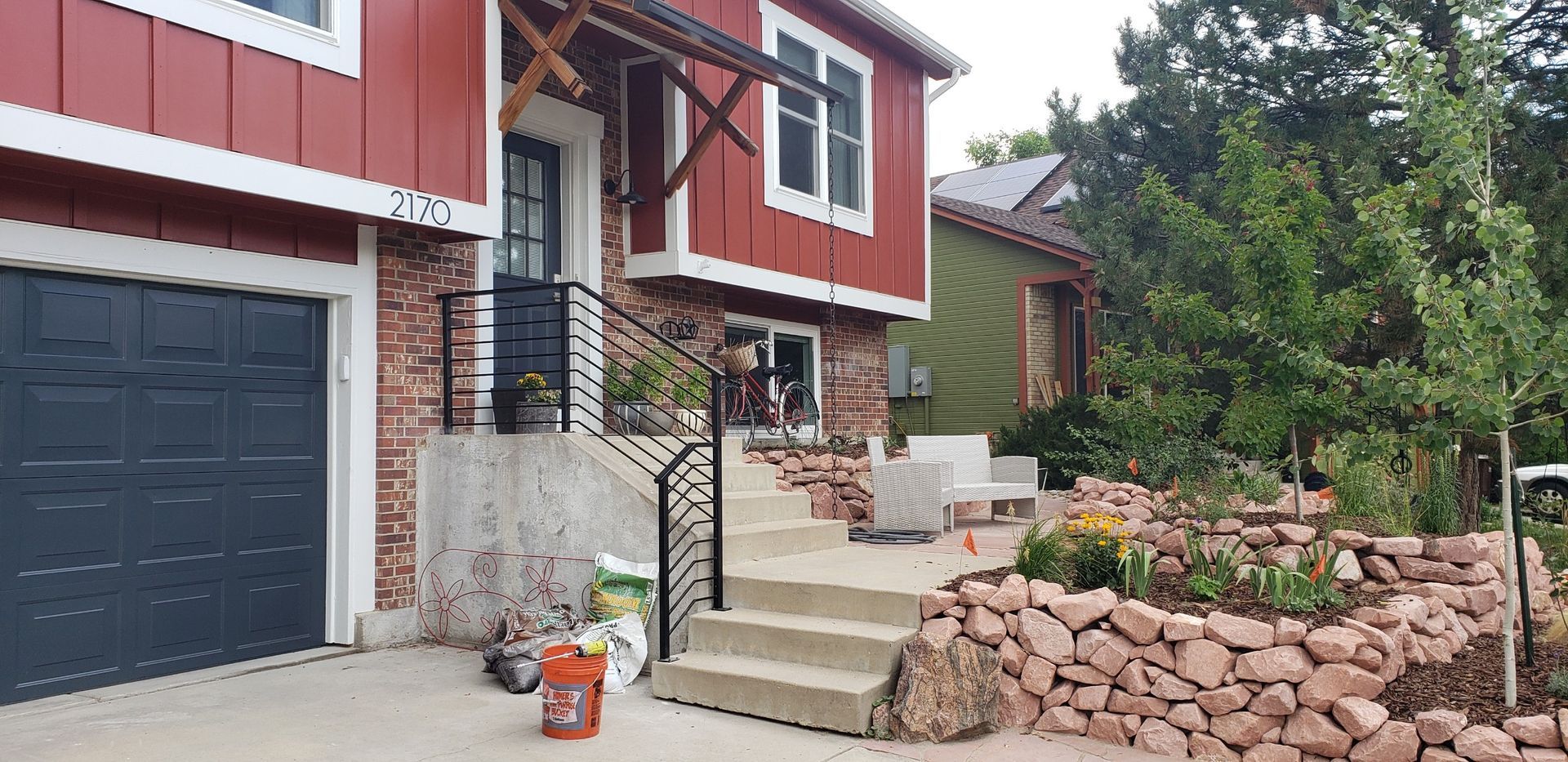 A red house with a black garage door is sitting next to a stone wall.