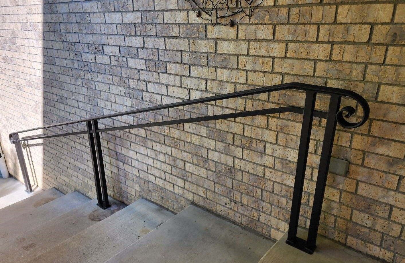 A black railing is against a brick wall next to a set of stairs.