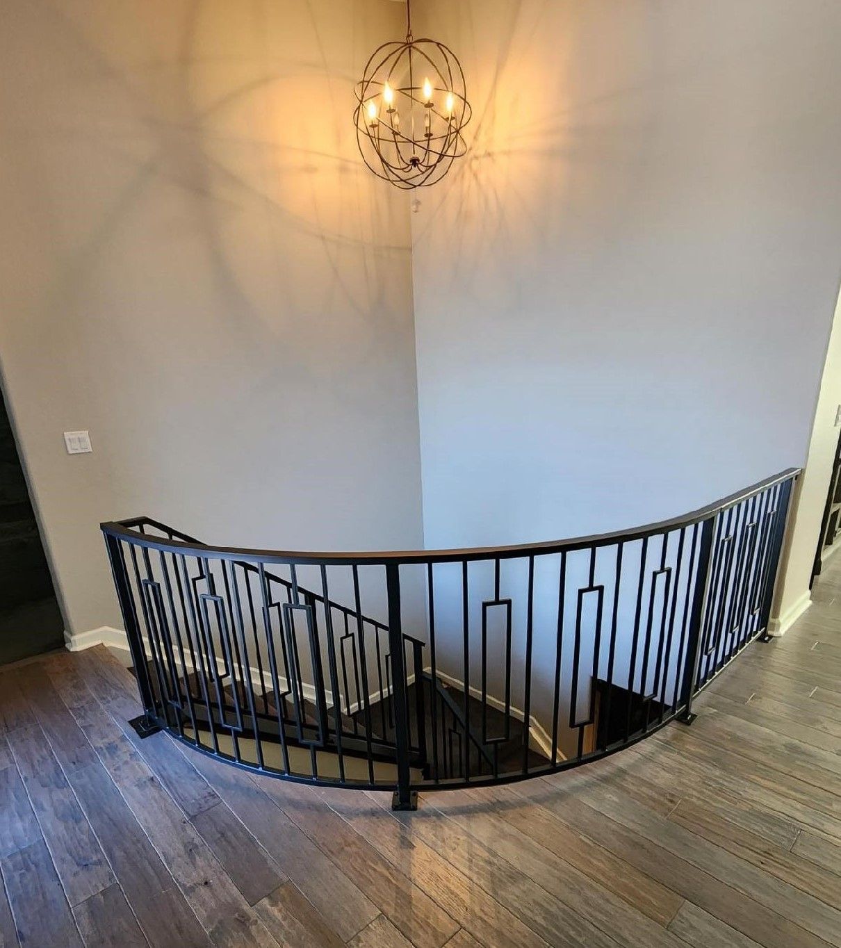 A staircase with a wrought iron railing and a chandelier hanging from the ceiling.