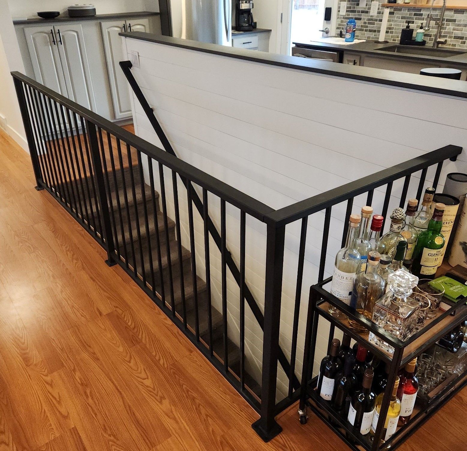A staircase with a black railing and a shelf with bottles of alcohol on it