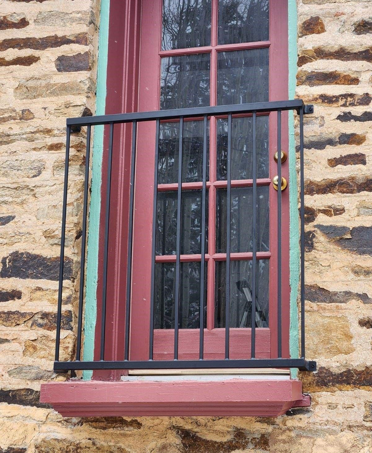A red window with a black railing on a stone wall