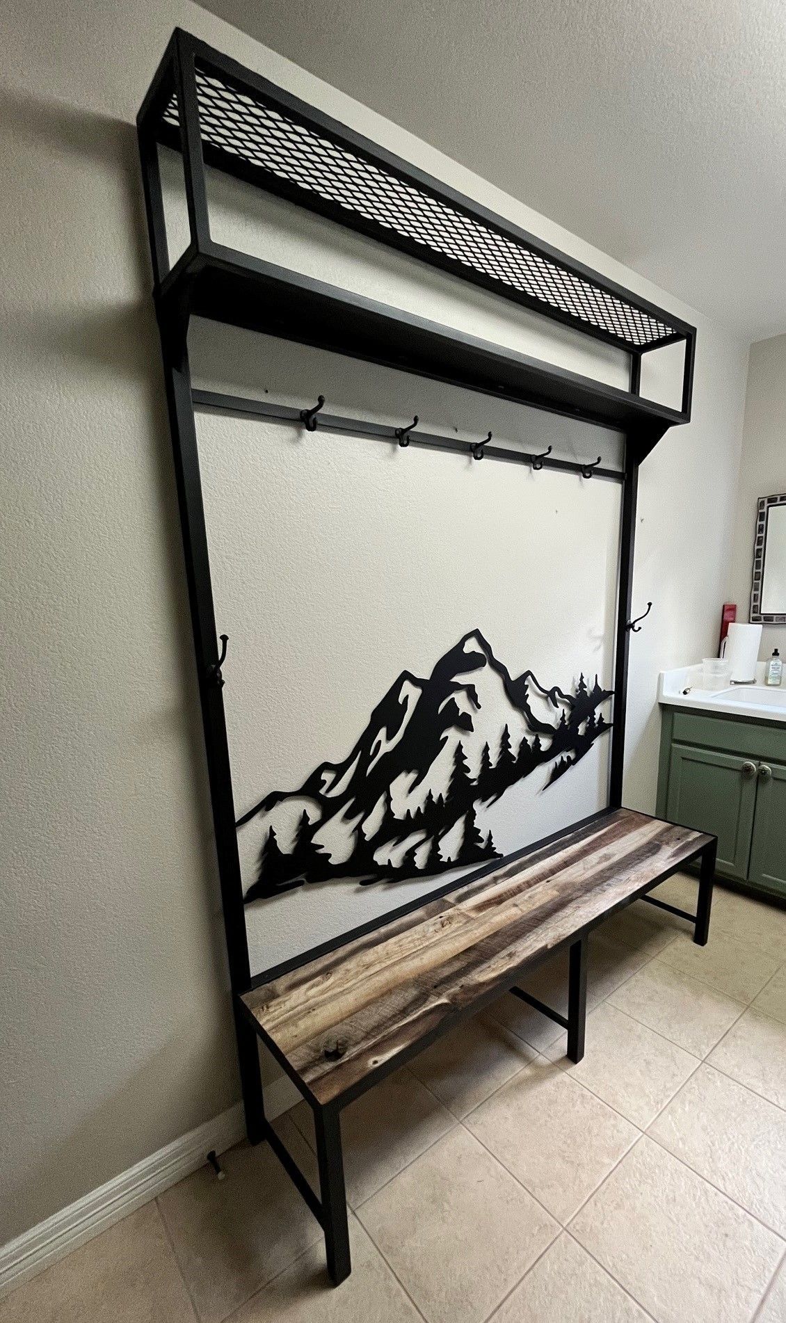A hallway with a bench and a coat rack with a mountain painting on the wall.