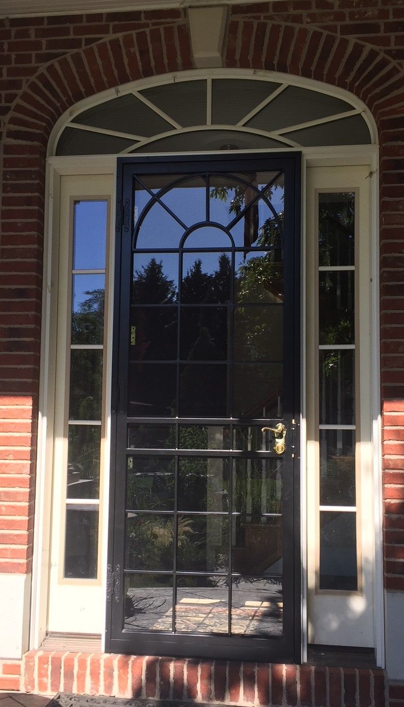 A black screen door is on a brick building.