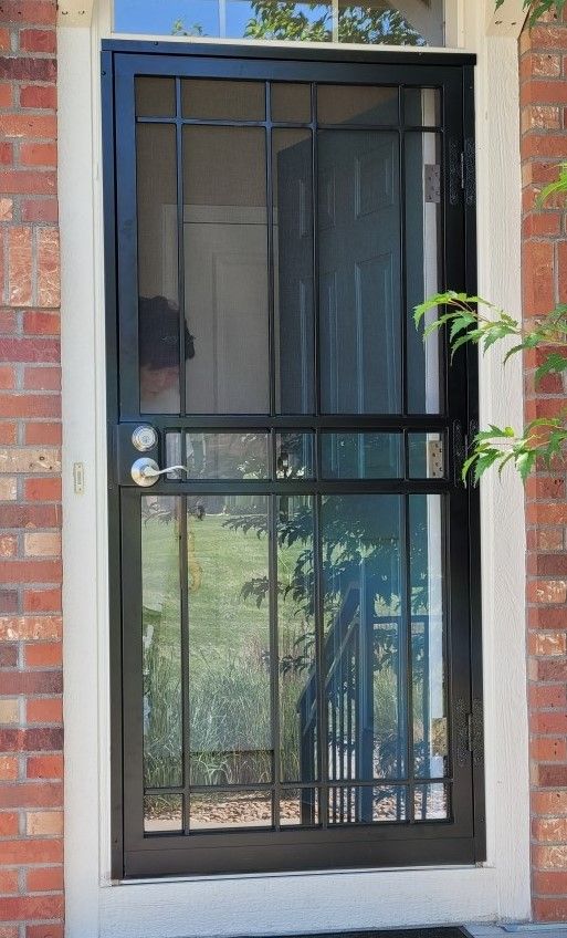 A black screen door is on a brick building.