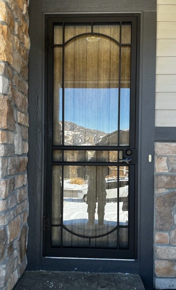 A black door with a screen on it is on a stone wall.