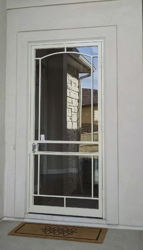 A white screen door with a welcome mat on the floor.
