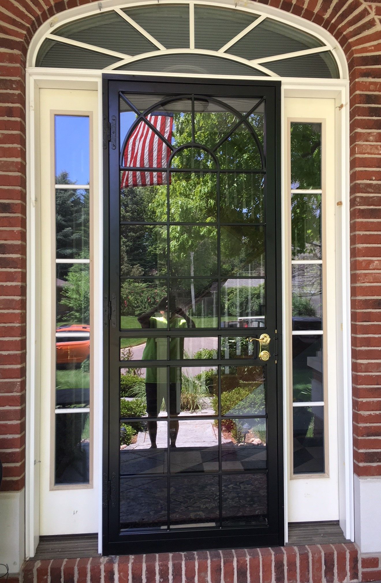 A black screen door is on a brick building.