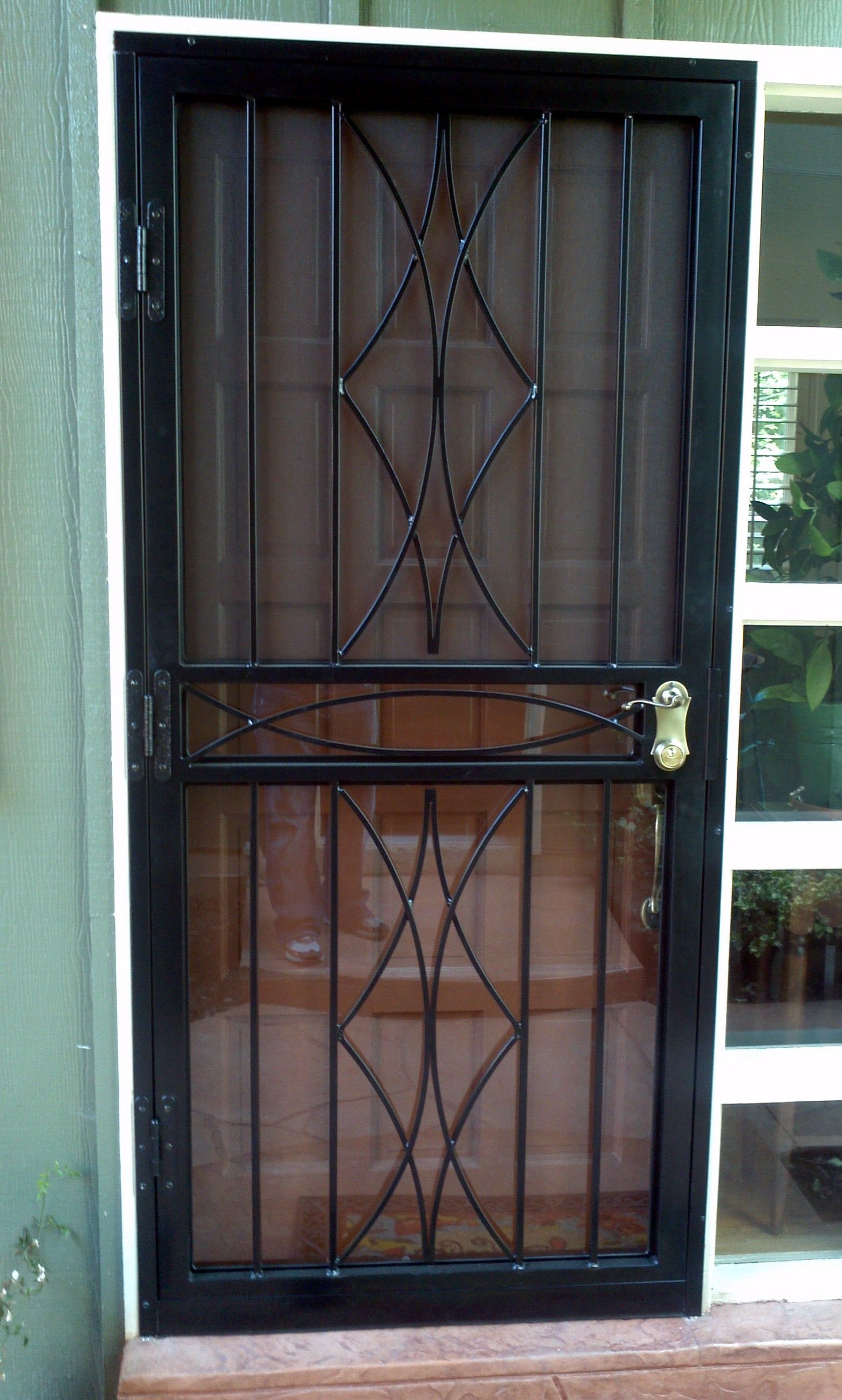 A black door with a wrought iron design on it is sitting next to a window.