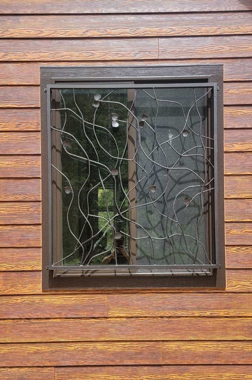 A window with a wrought iron grill on a wooden wall.