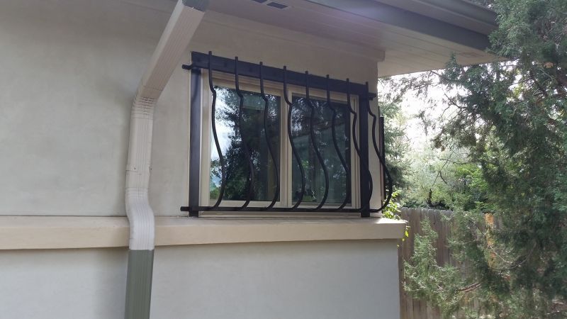A window on the side of a house with a wrought iron fence around it.