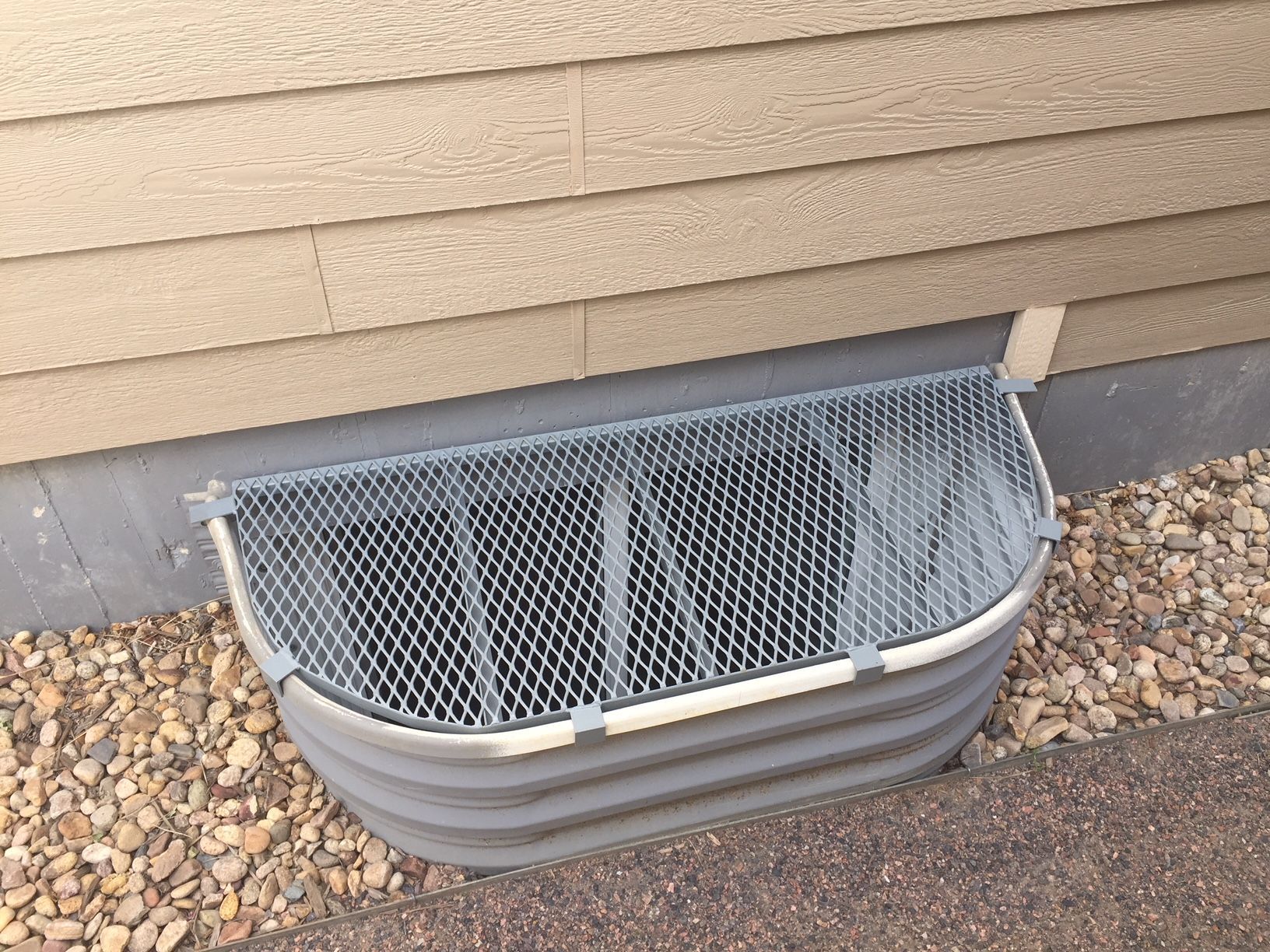 A window well next to a house with a mesh cover