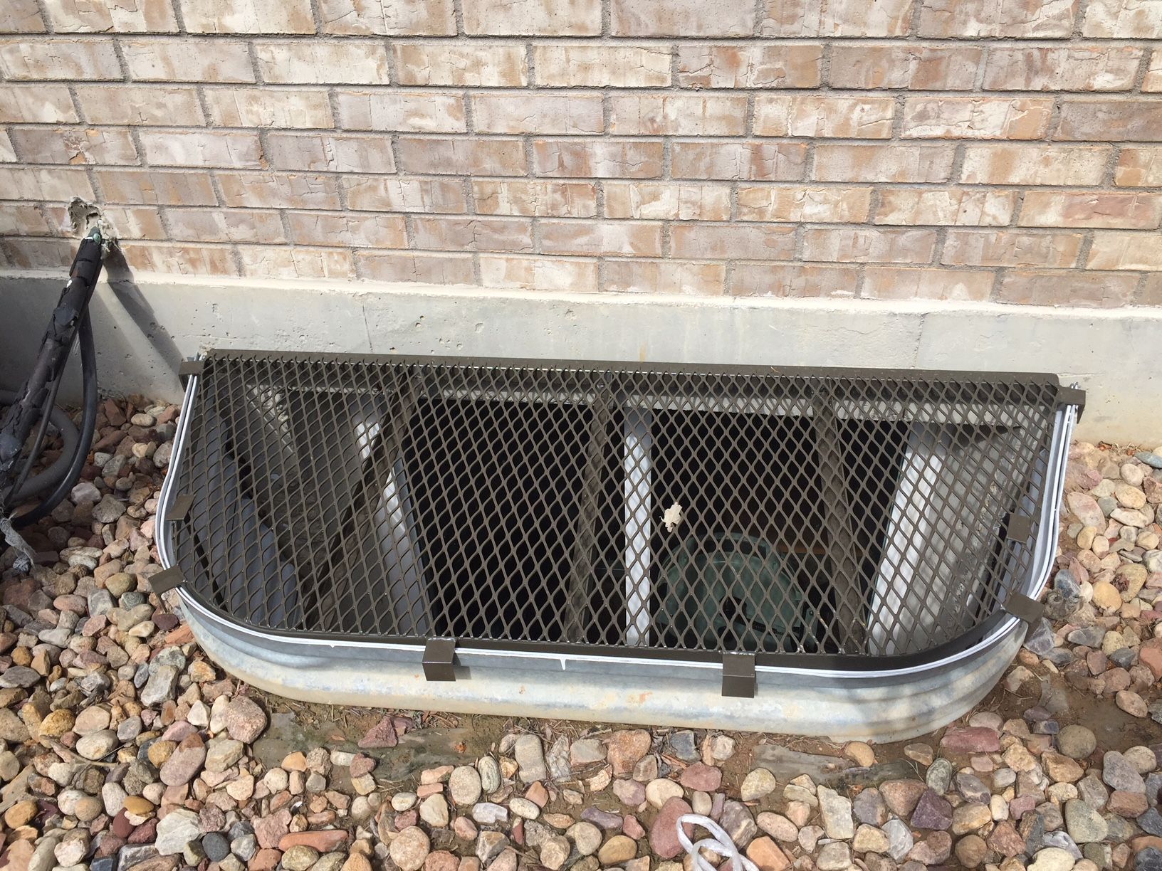 A brick wall with a metal grate over a window well.