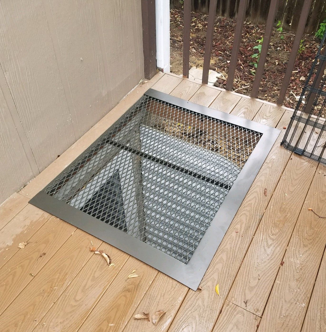 A metal grate is sitting on a wooden deck next to a railing.