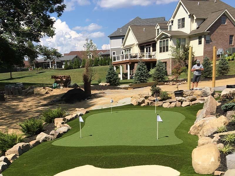 Backyard putting green with rocks and houses in the background, two people standing nearby.
