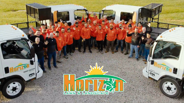 Large group in orange shirts posing by white trucks with open trailers; Horizon logo centered in front