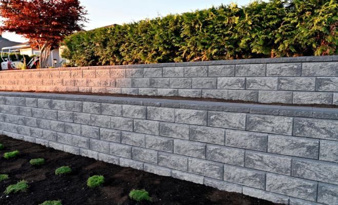 Stone retaining wall with gray blocks beside a landscaped garden and hedge at sunset