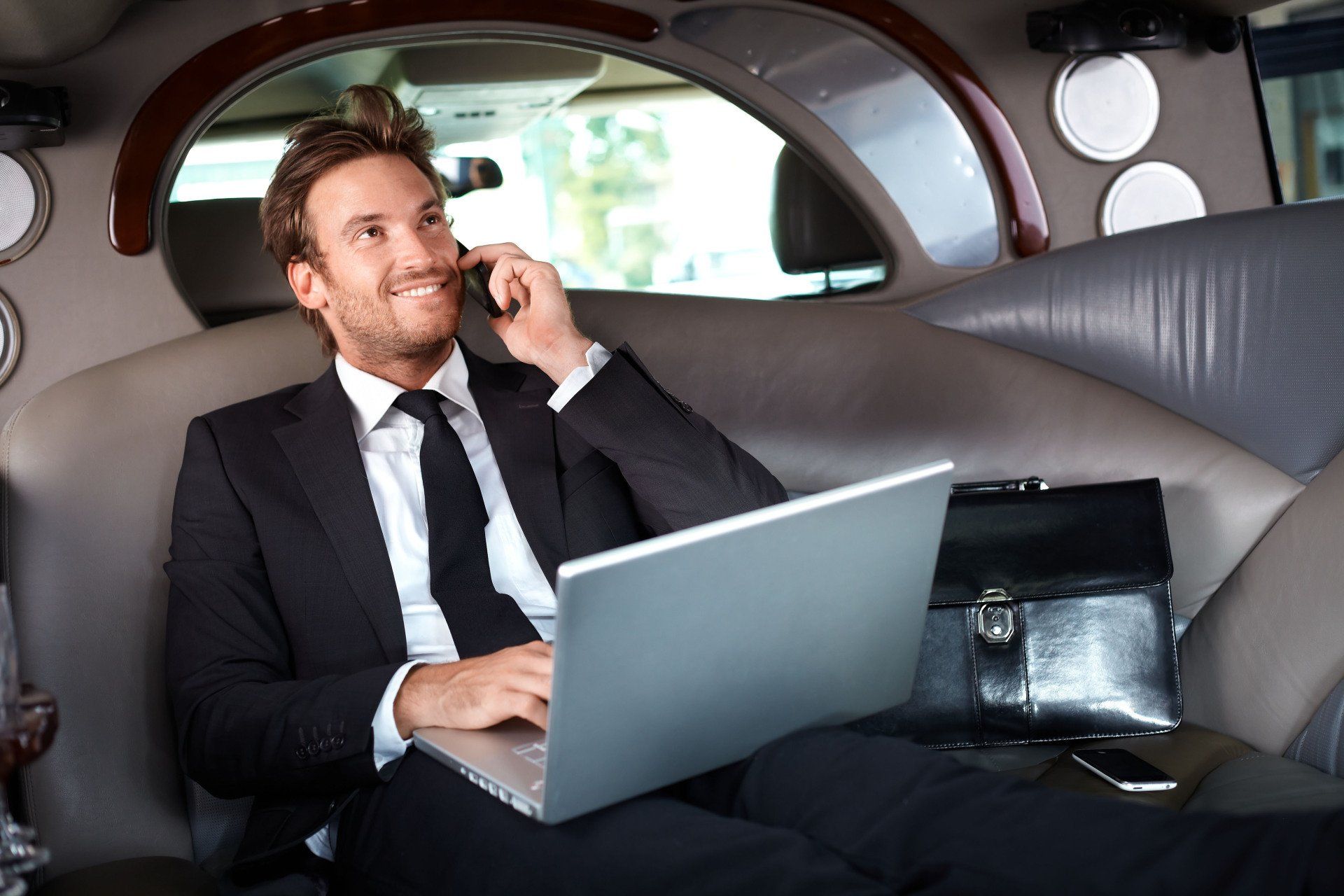 Man in suit, using laptop and phone in a limousine.