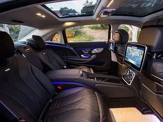 Luxurious car interior: black leather seats, rear entertainment screens, open sunroof, ambient lighting.