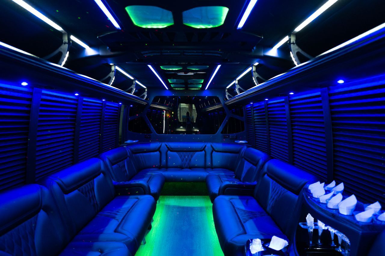 Interior of a party bus, black leather seating, illuminated with blue and green LED lights.