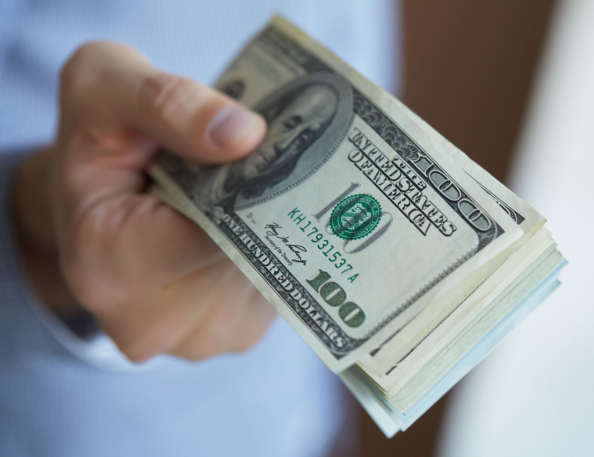 Hand holding a stack of $100 bills, offering money.