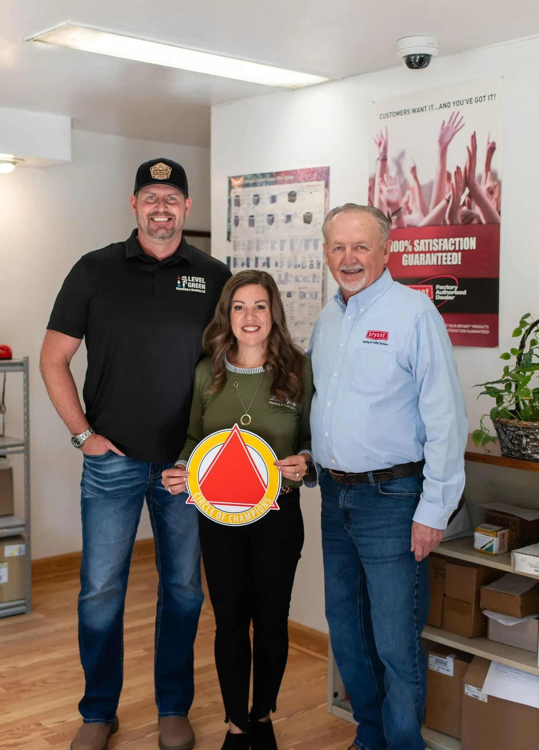 Three people indoors, holding a reflective orange safety triangle. Office setting with a poster and boxes.