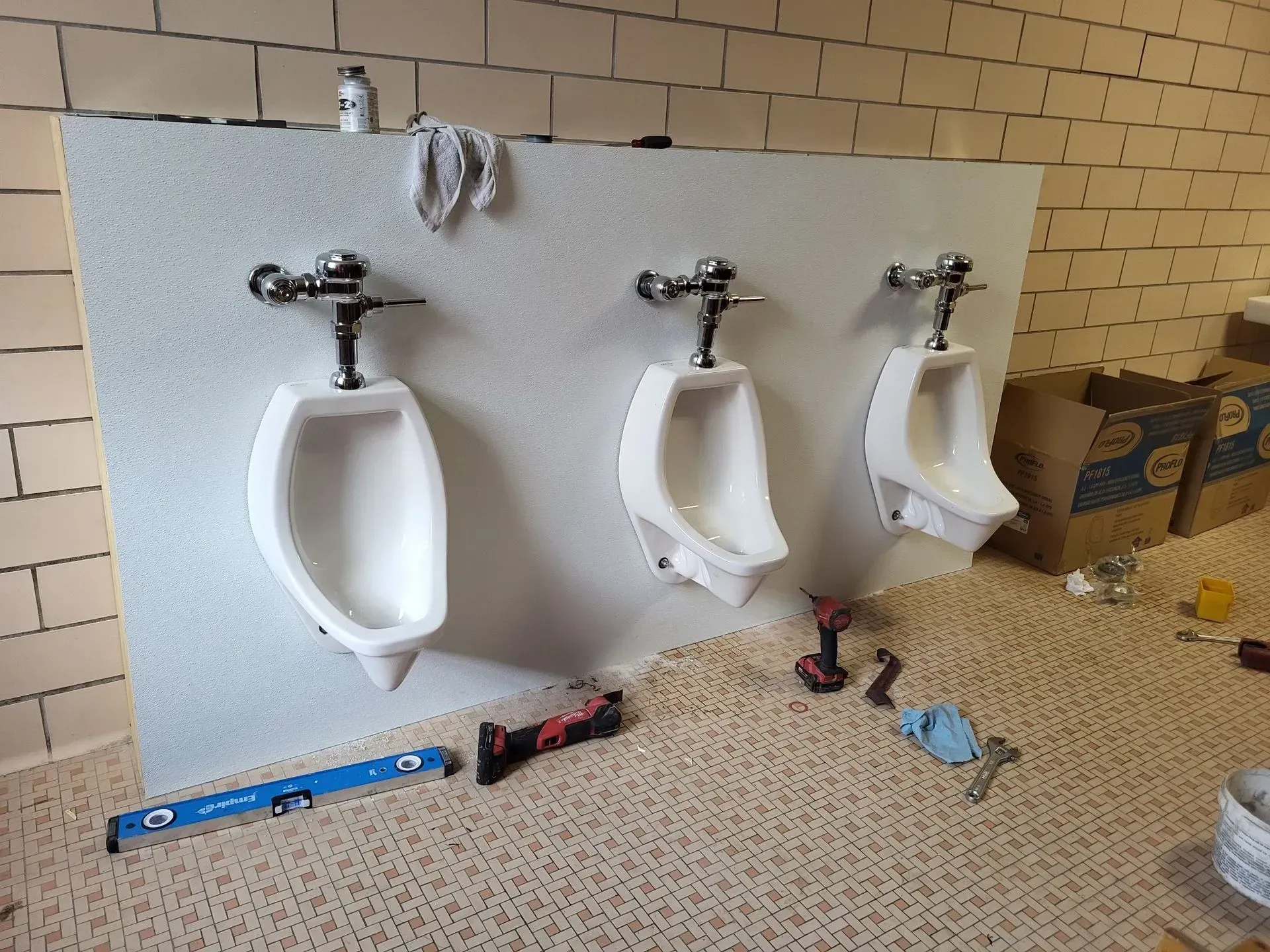 Three urinals in a bathroom, in various stages of installation, against a textured white wall.