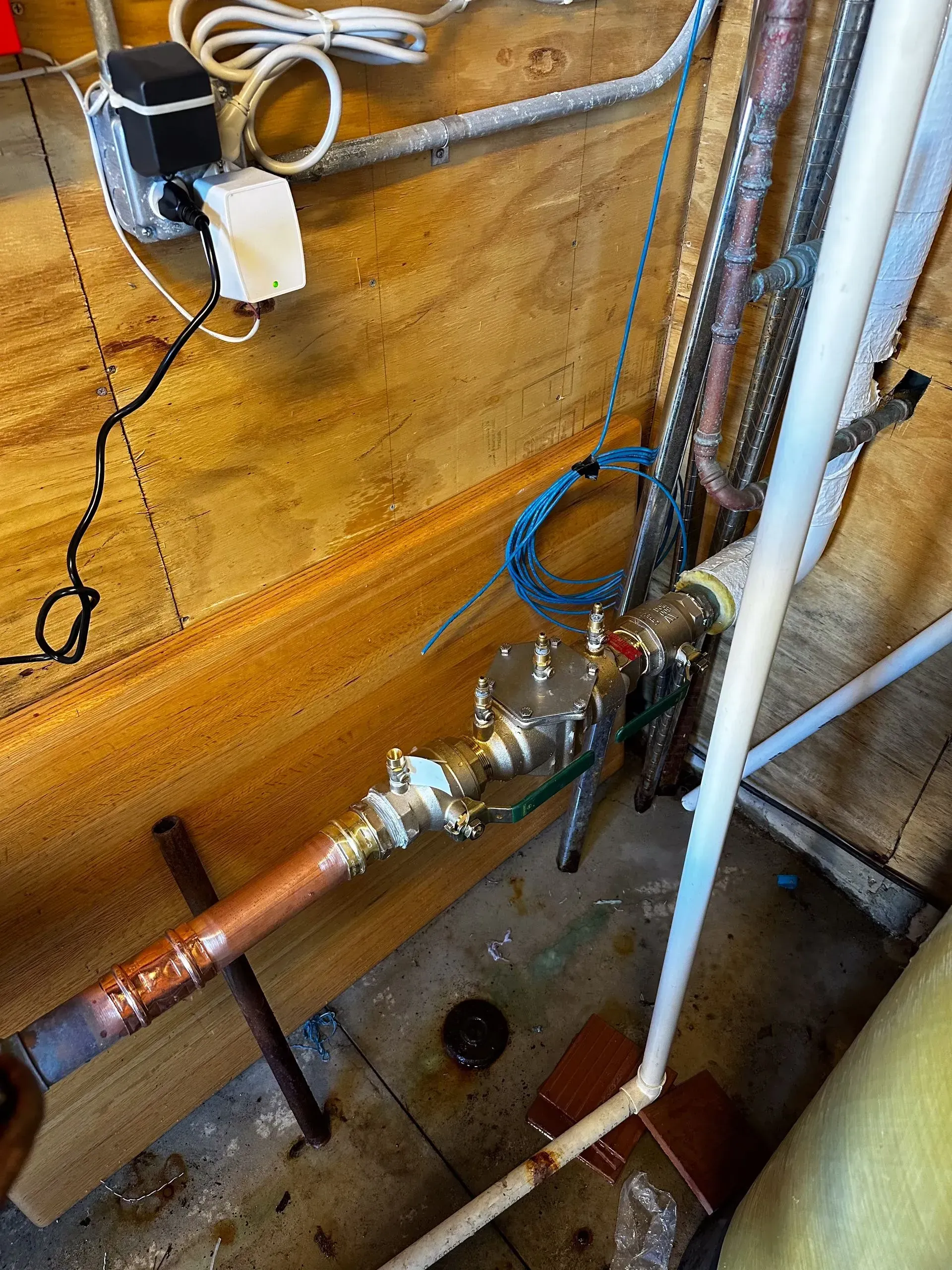 Plumbing pipes and valves in a basement setting with copper and PVC pipes.