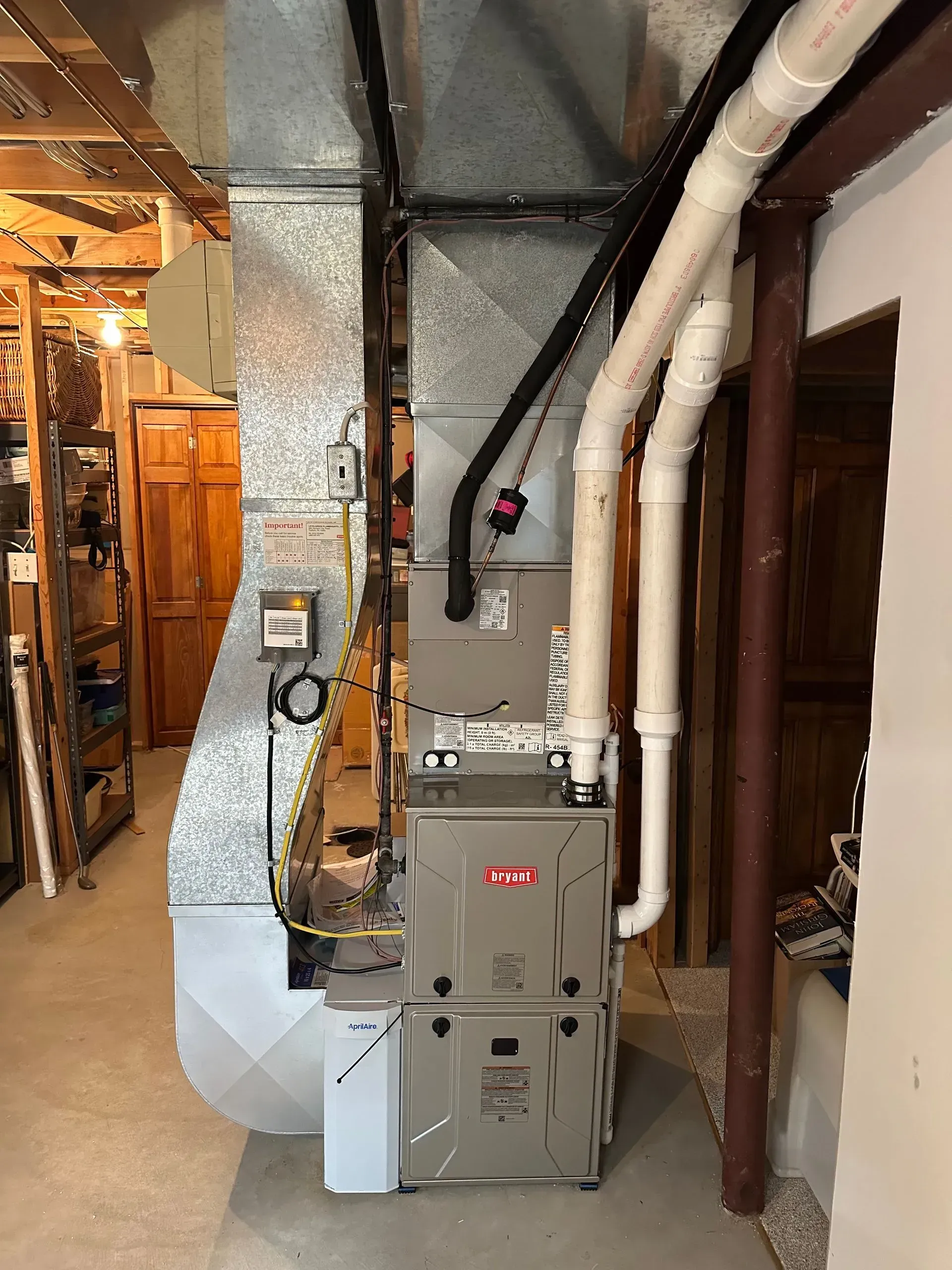 Furnace and ductwork in a basement. Gray metal furnace with white PVC pipes and silver ducting.