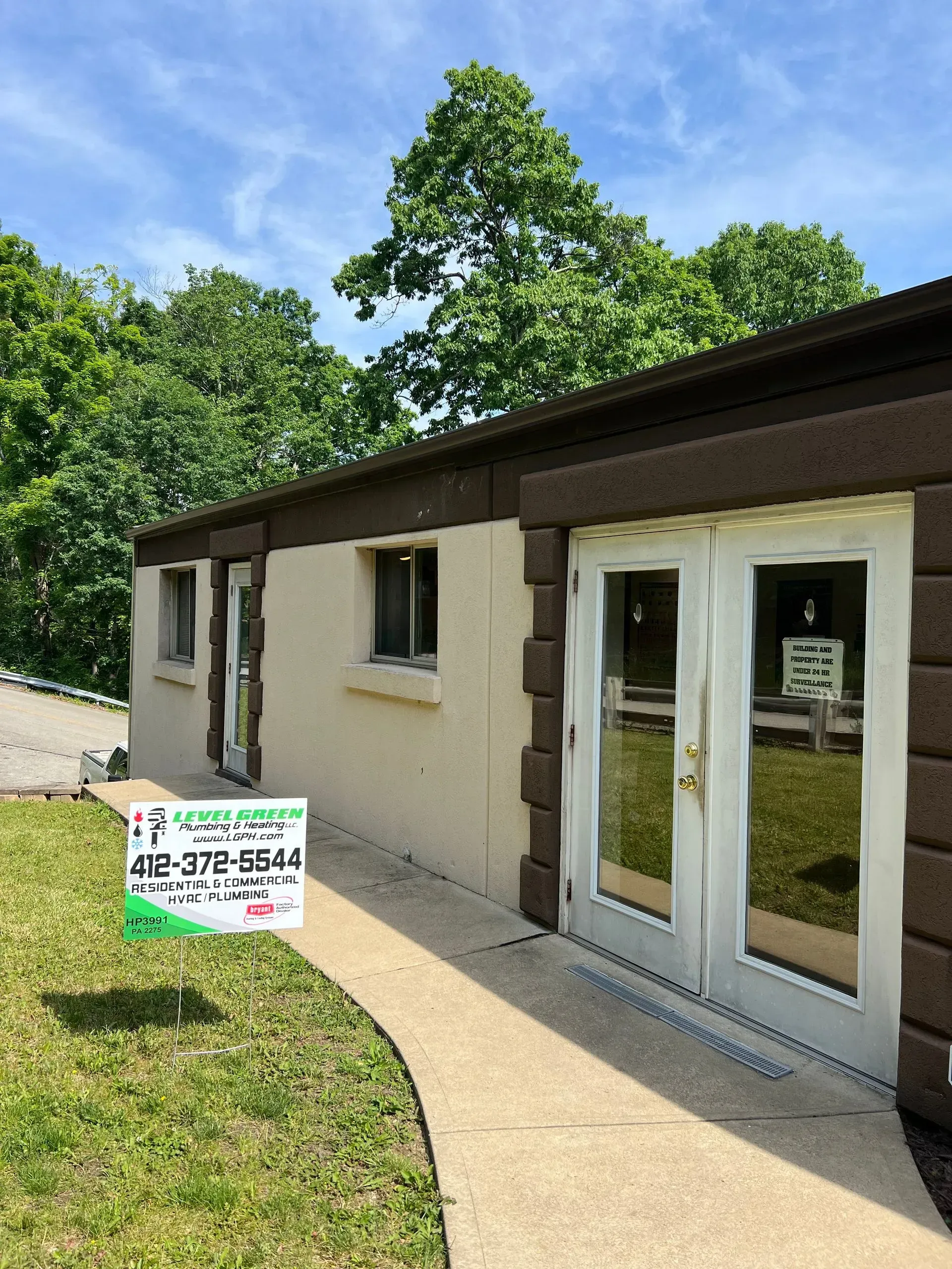 Tan building with brown trim and double doors, a pathway leads up to it. Sign in front.