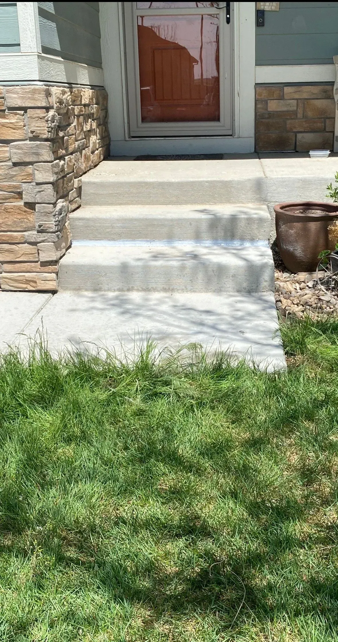 Concrete steps leading up to a front door, with grass in the foreground and a stone wall on the left.