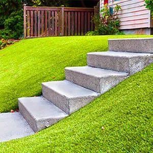 Concrete steps built into a grassy hillside, leading up. Fence and building visible in background.