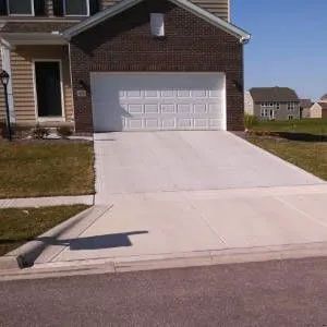 A newly poured concrete driveway leads to a two-car garage of a brick-faced house on a sunny day.