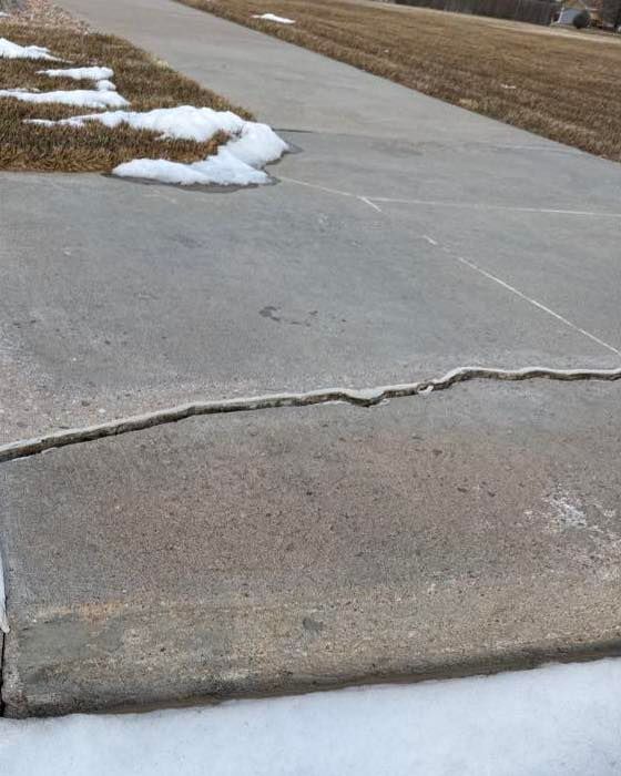 Concrete pathway with a crack being measured with a gauge. Stone planter is in the background.