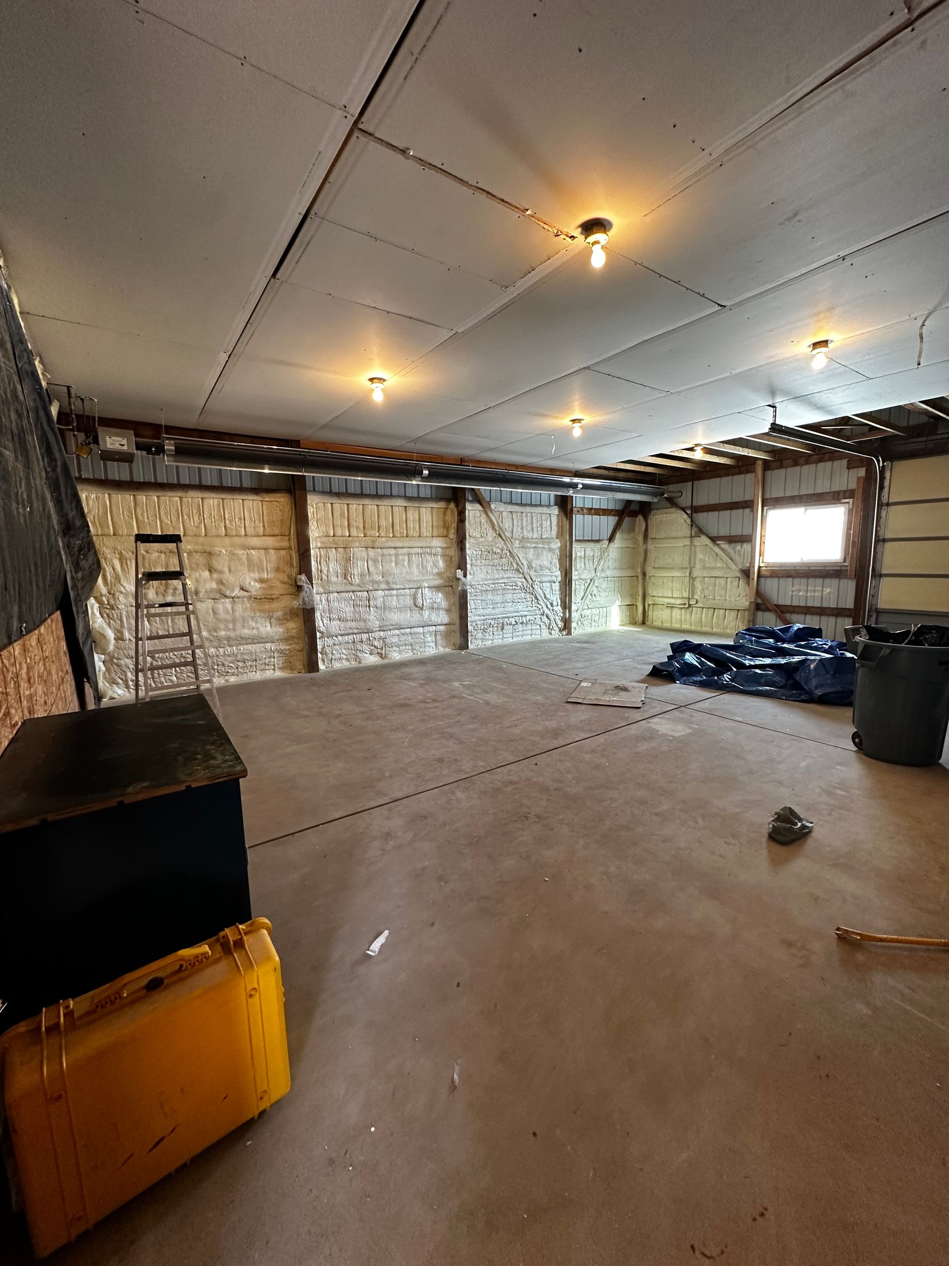 Interior view of a building under renovation, exposed beams, unfinished walls, concrete floor, overhead lights, storage containers.