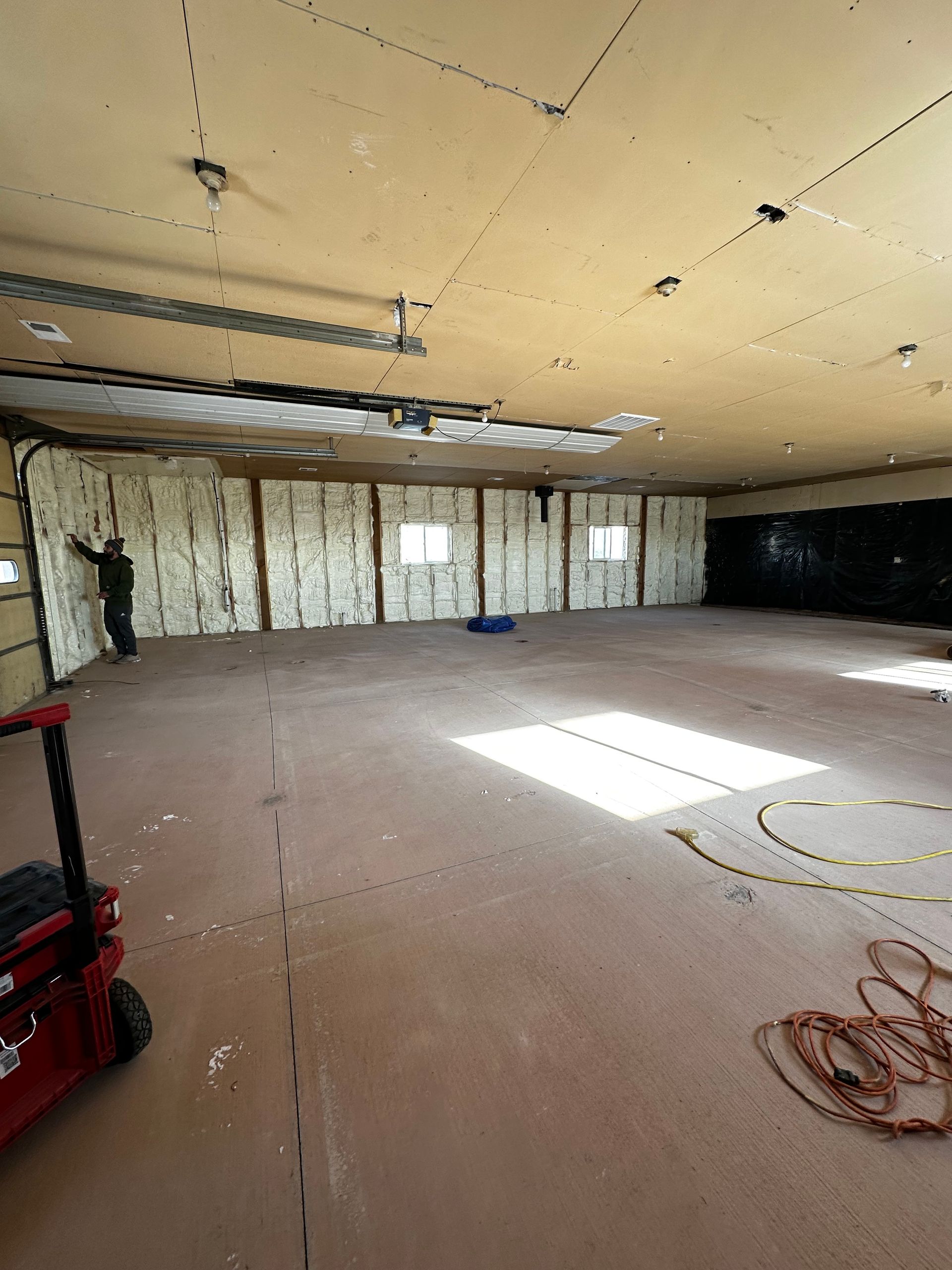 Interior of a garage being renovated; walls and ceiling have insulation installed. A person works on the wall.
