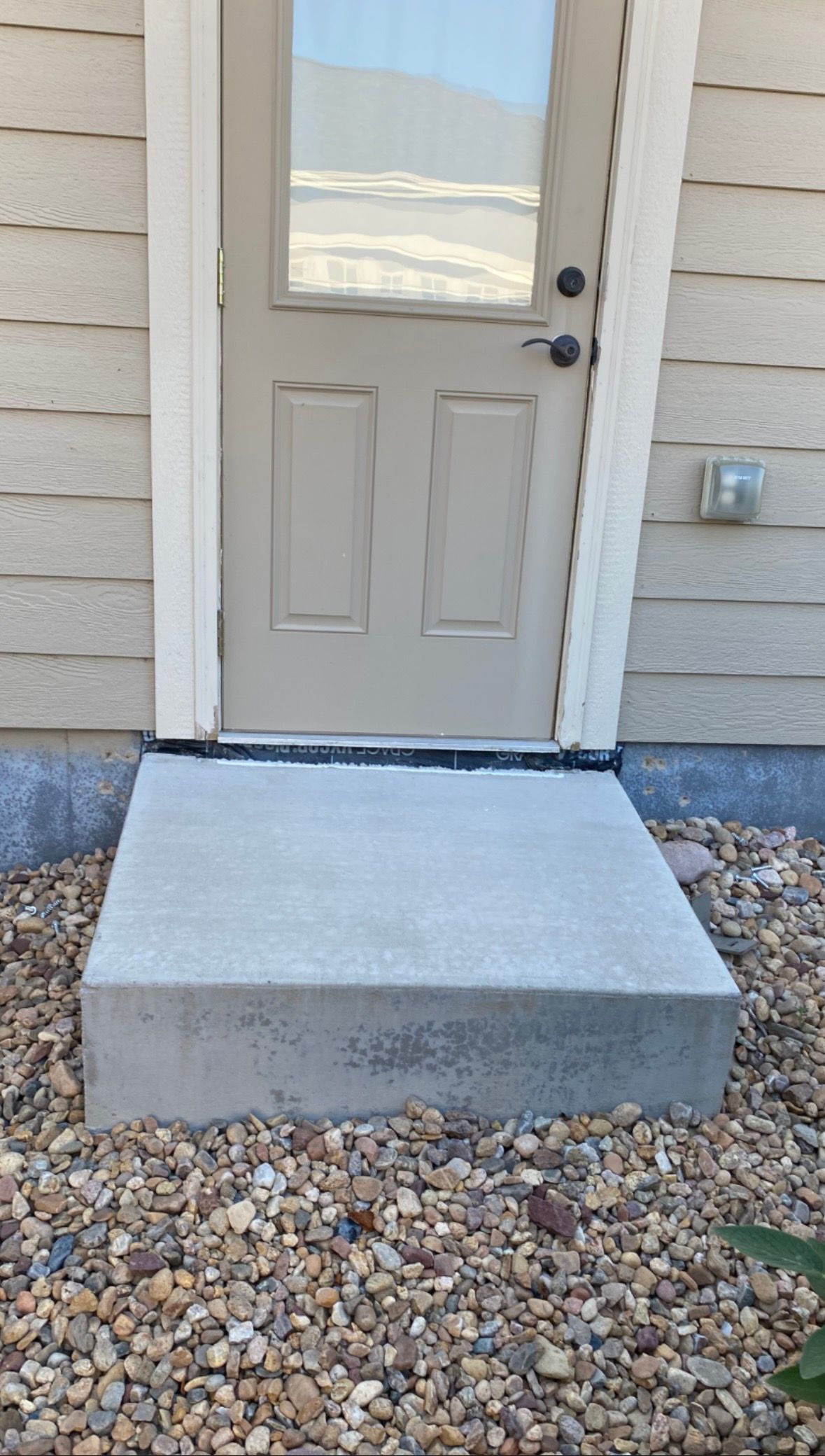 Concrete step leading to a white door with glass panel, gravel ground.