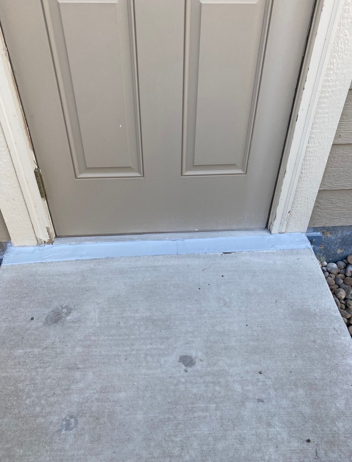 Tan door with concrete step, a small gap between door and step.