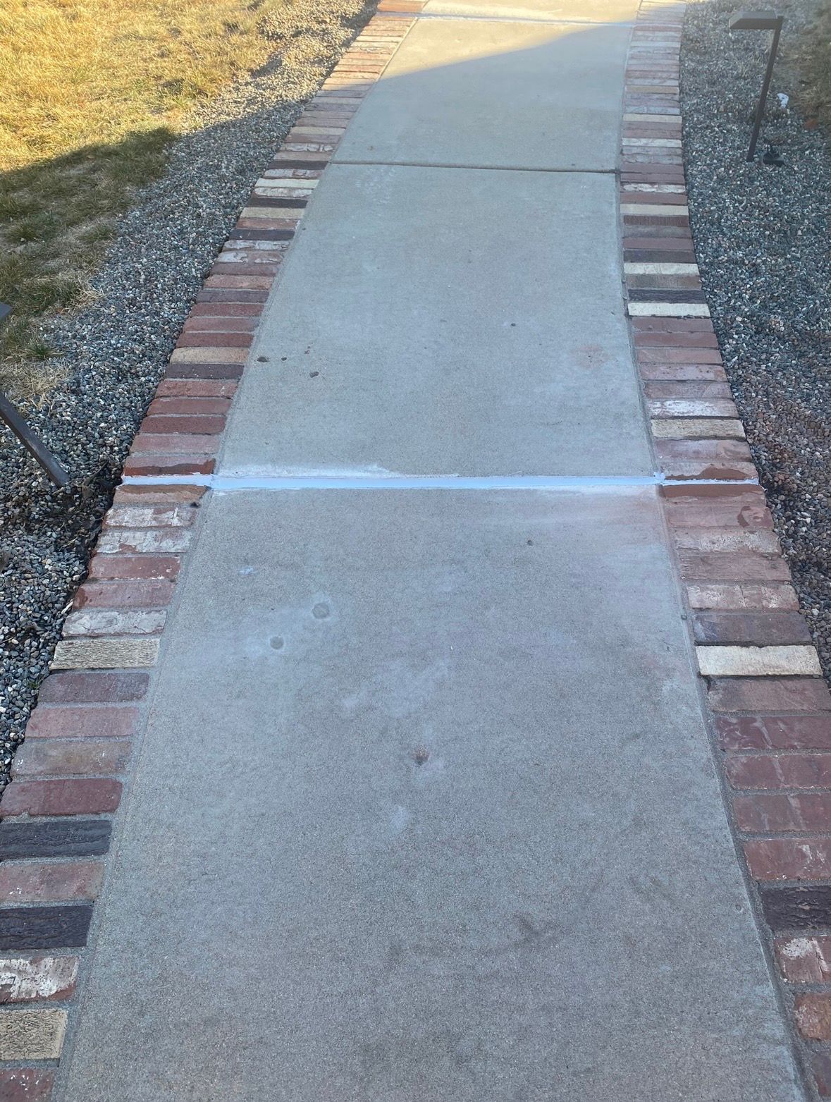 A stamped concrete driveway with a portion of a black vehicle, next to green grass.