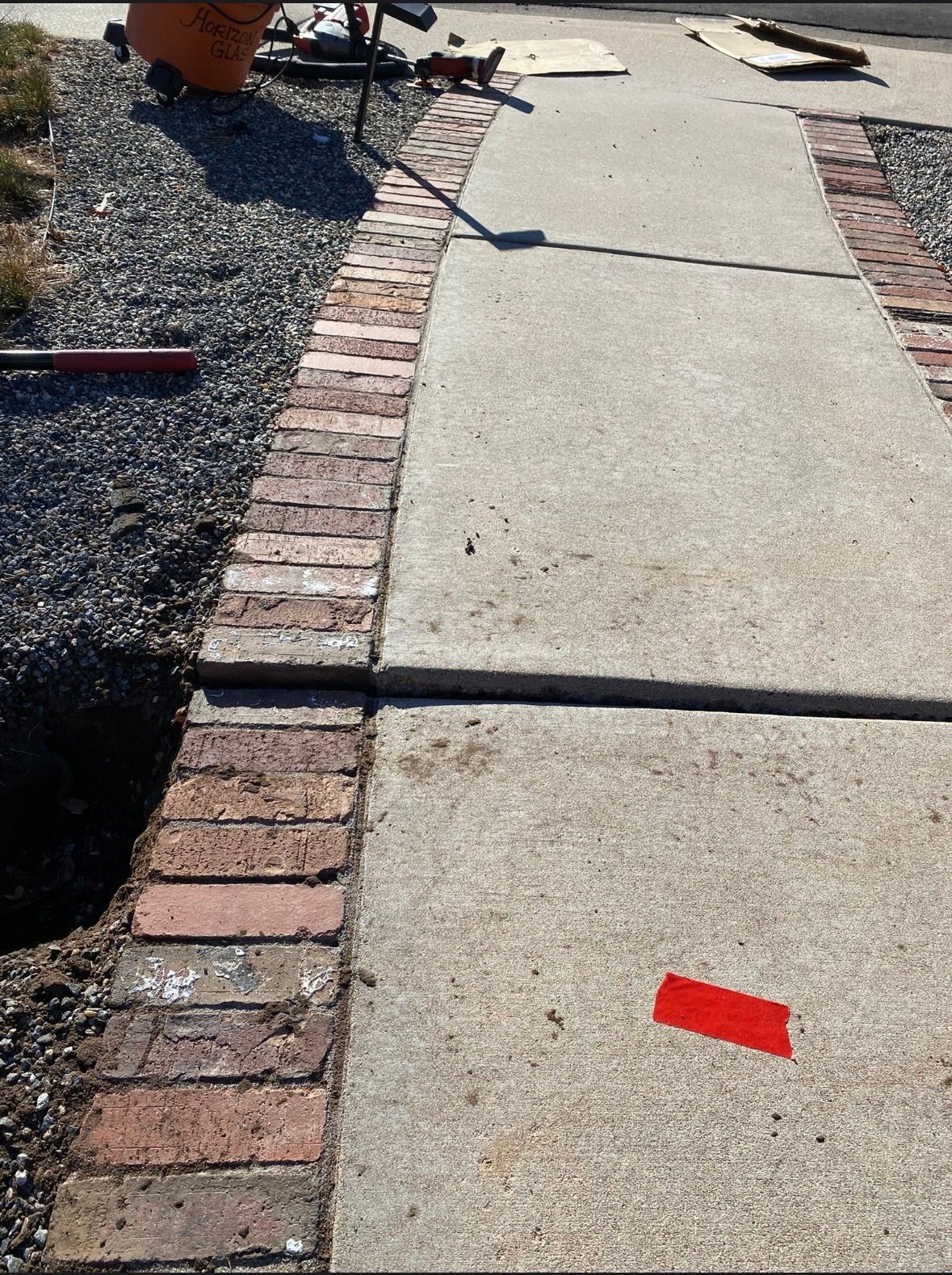 A yellow tape measure is placed vertically over a crack in a concrete patio, showing about 3 inches.