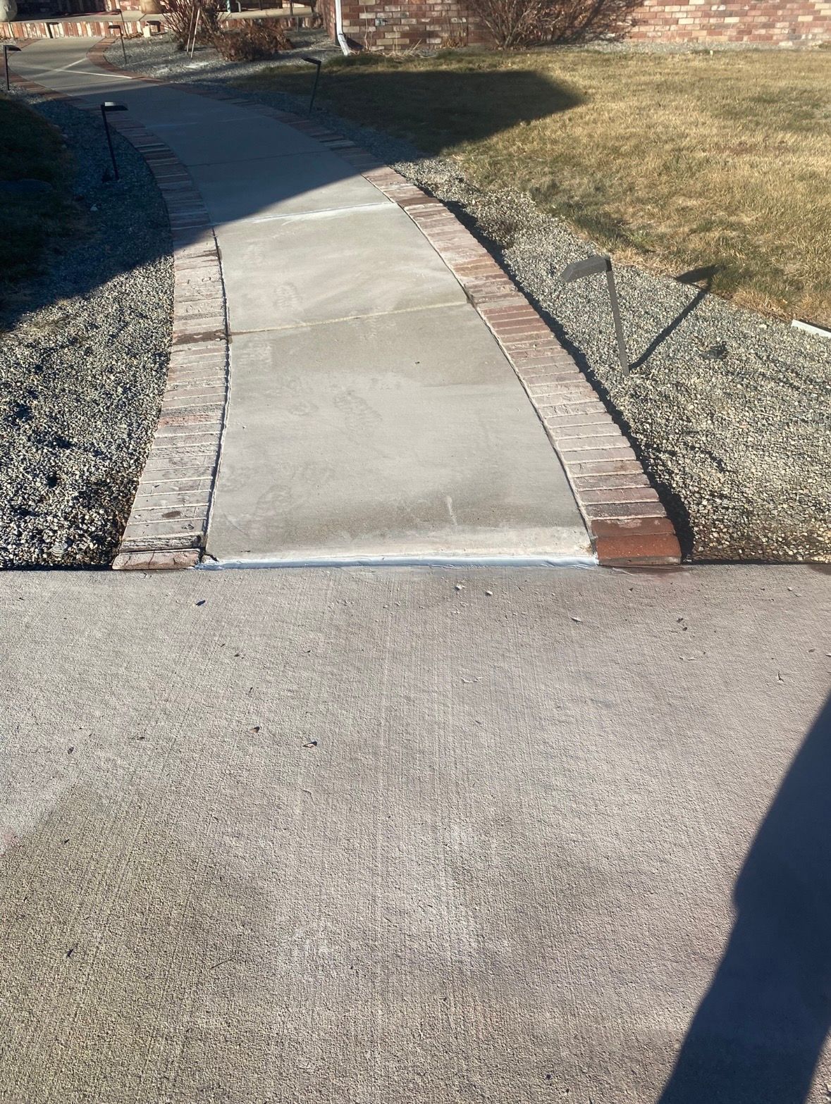 Concrete walkway with brick border and gravel bed, leading from a driveway.