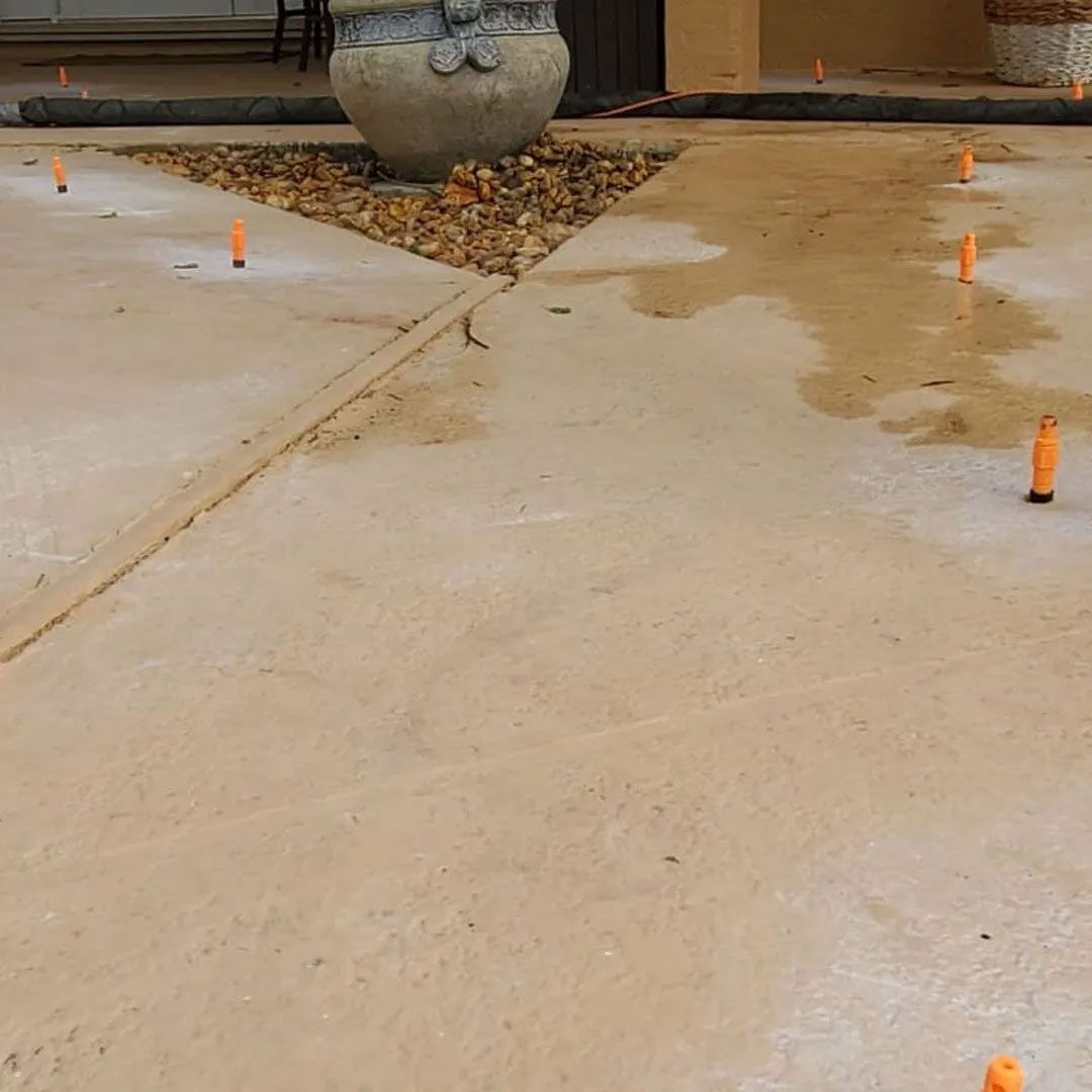 Wet concrete surface with orange marker stakes. A large decorative pot sits on gravel.