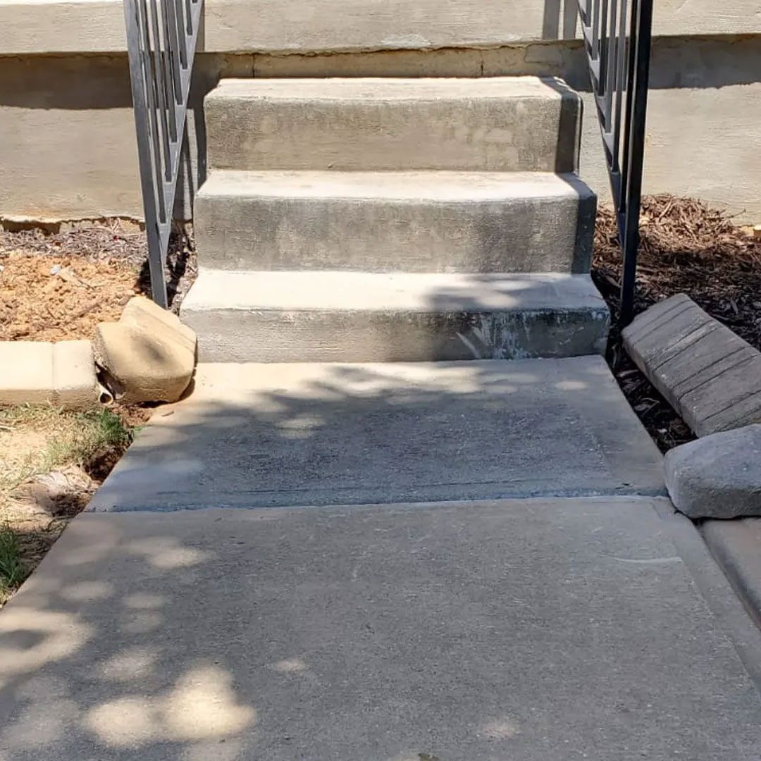 Concrete steps leading to a building entrance; black railing on either side.
