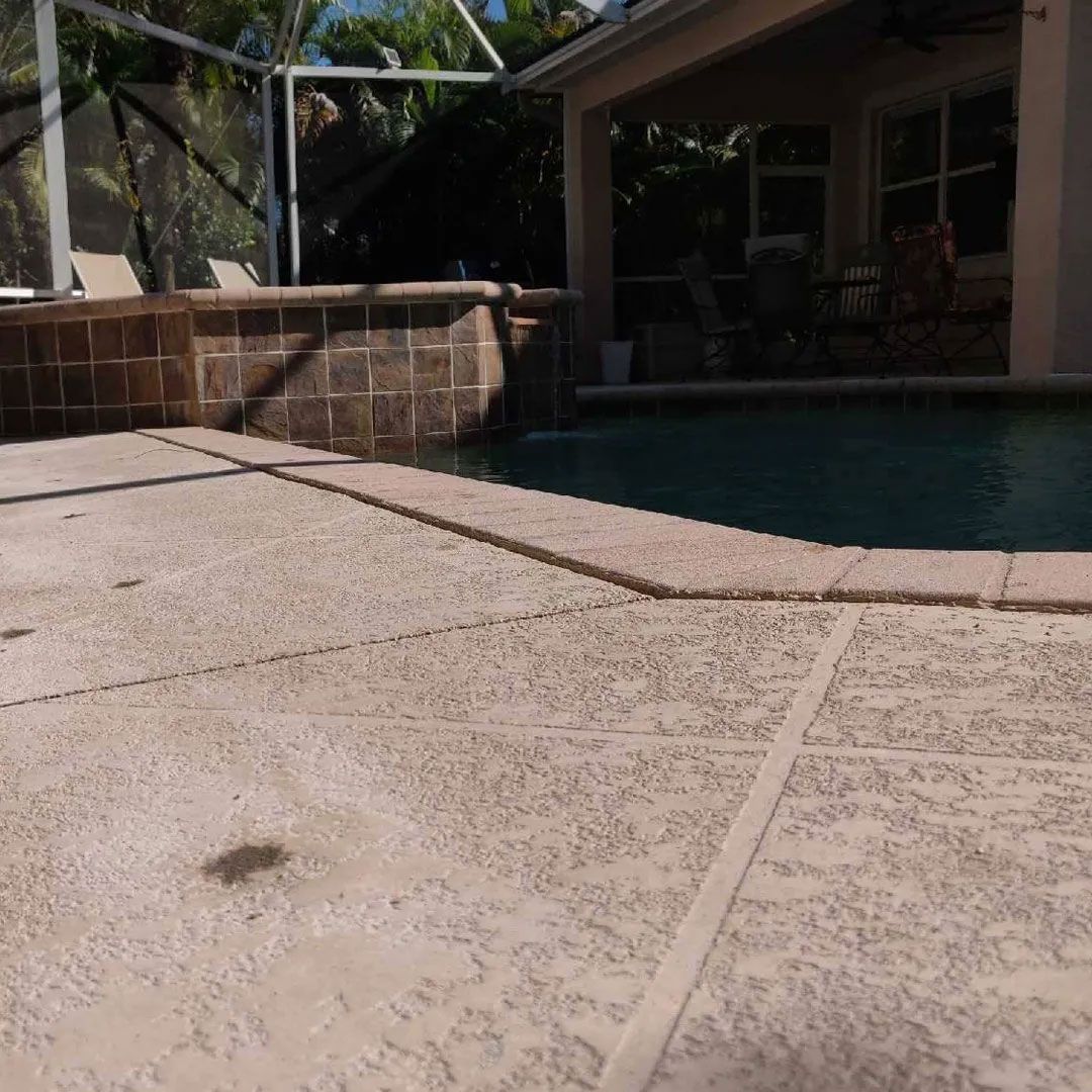 A concrete patio next to a pool with a brick wall and a covered outdoor area.