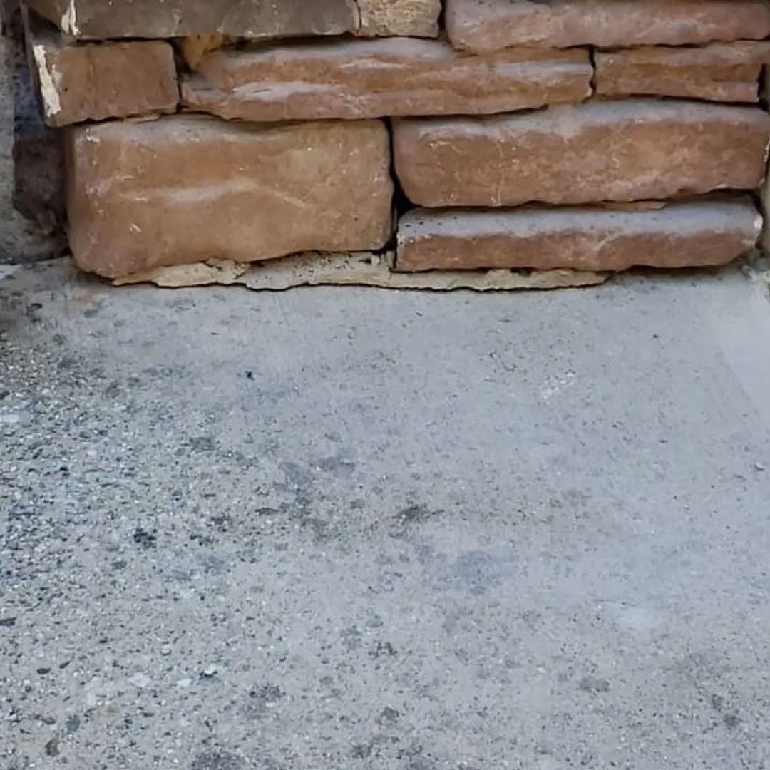 Stone wall base on concrete surface, with a mix of tan and gray hues.