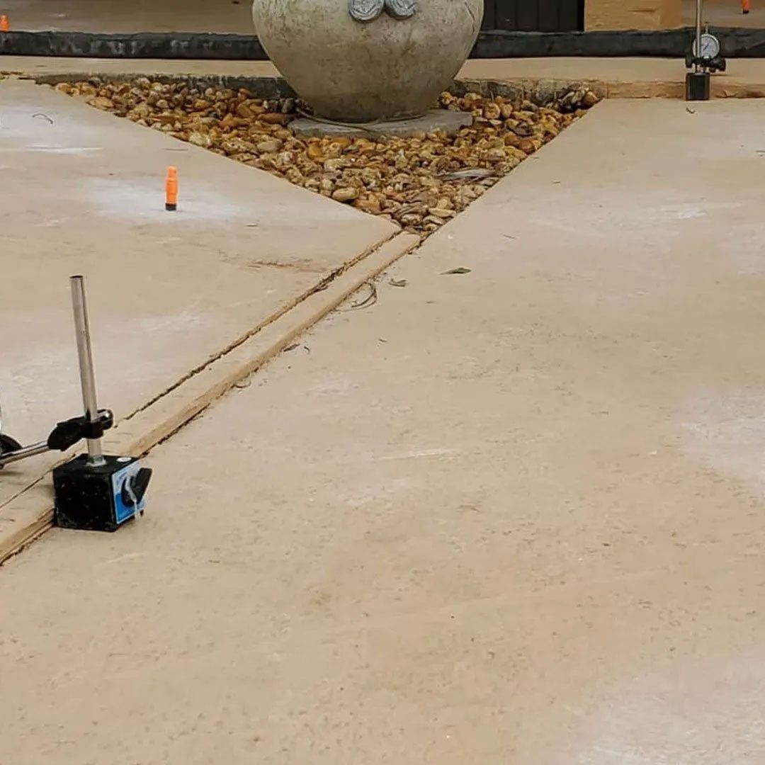 Concrete pathway with a crack being measured with a gauge. Stone planter is in the background.