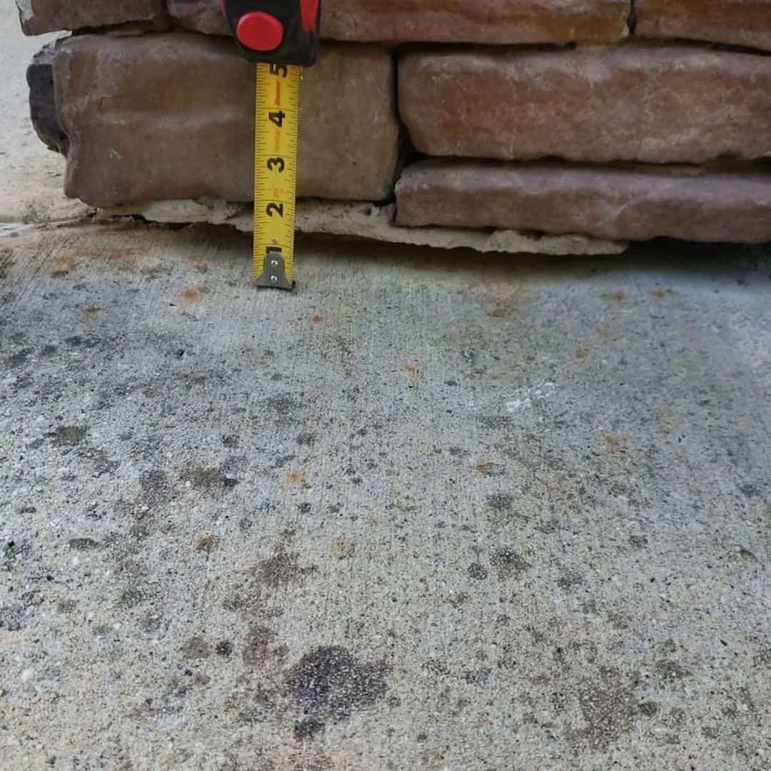 Tape measure next to a stone wall, showing height measurement of approximately 3 inches.