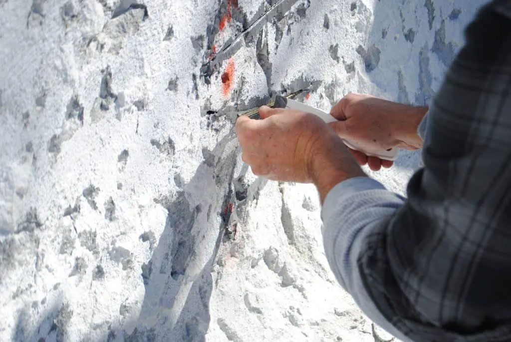 Person using a tool to work on a white rock face, presumably for climbing.
