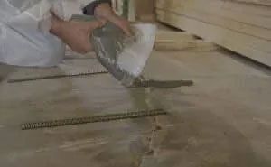 Person pouring cement onto a floor with metal rods, indoors.